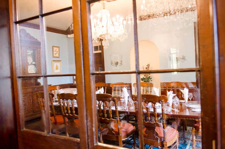 Elegant dining room viewed through glass doors with wooden furniture, chandelier, and formal place settings