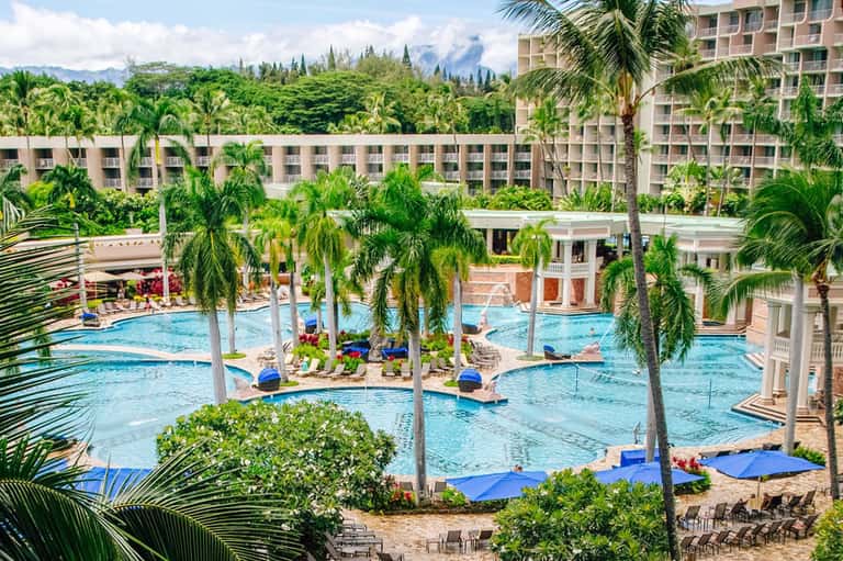 Aerial view of large resort pool complex with multiple pools, palm trees, and beige buildings
