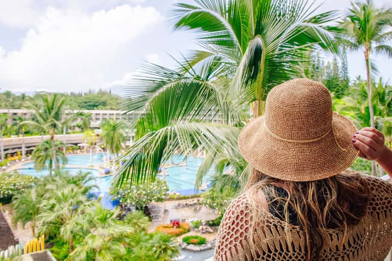 Woman in straw hat overlooking lush resort grounds with pools and palm trees