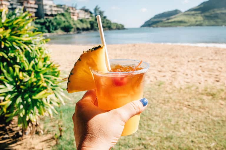 Tropical beach cocktail with pineapple garnish and straw held against scenic mountain backdrop