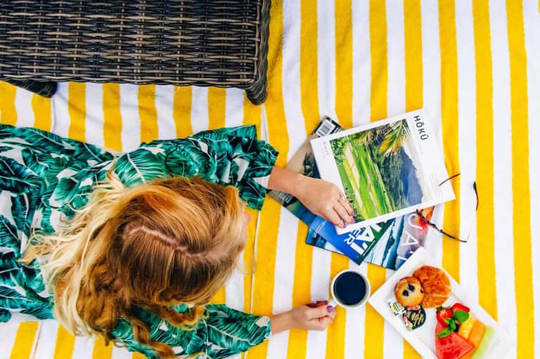 Overhead view of woman reading on yellow striped lounger with tropical snacks and beverage