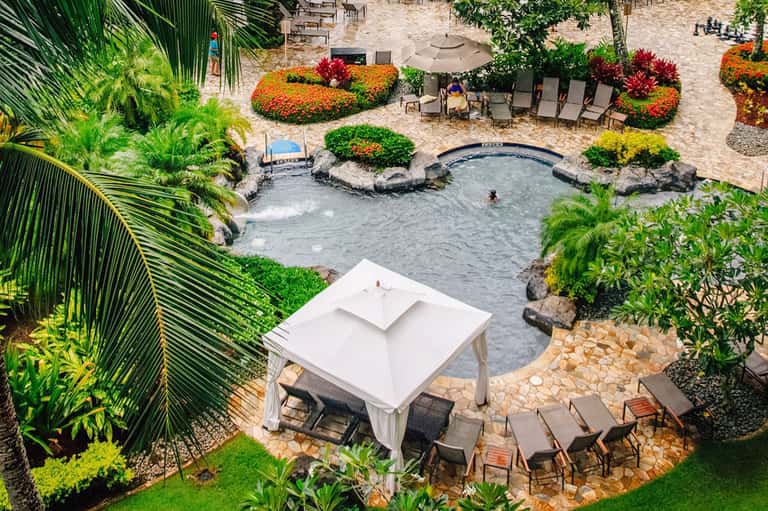 Aerial view of tropical resort with natural hot spring pool, white cabana, lounge chairs, and lush gardens