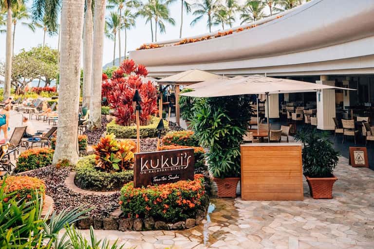Kukui's beachfront restaurant entrance with tropical flowers and shaded umbrellas
