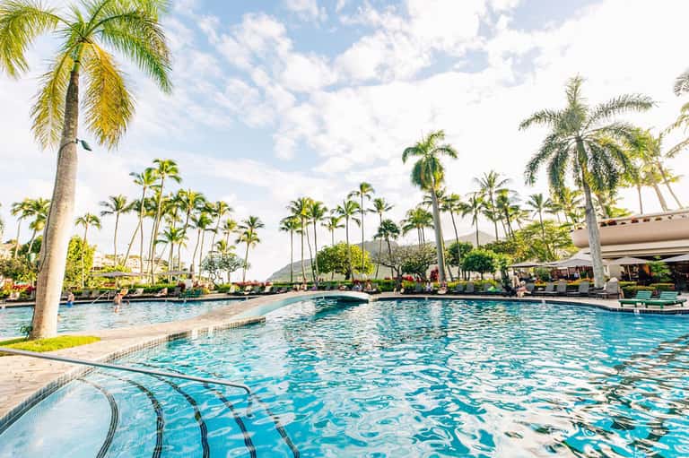 Large resort swimming pool surrounded by palm trees with mountains in tropical landscape background