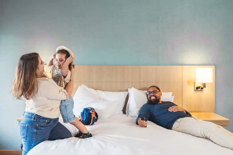 Family in modern hotel room with parents and child on bed with contemporary furnishings