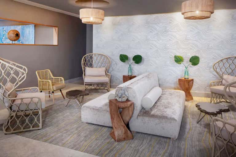 Modern spa lounge with white furniture, woven chairs, pendant lighting, and botanical wall décor
