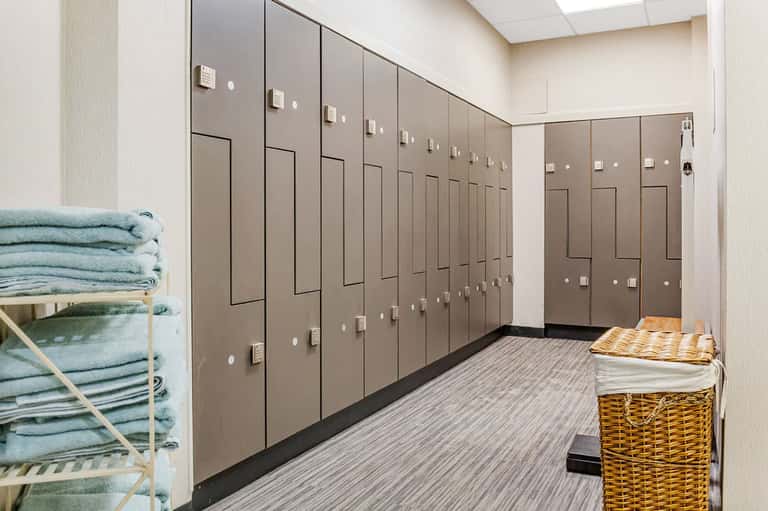 Locker room with rows of brown lockers, shelves with folded towels, and baskets
