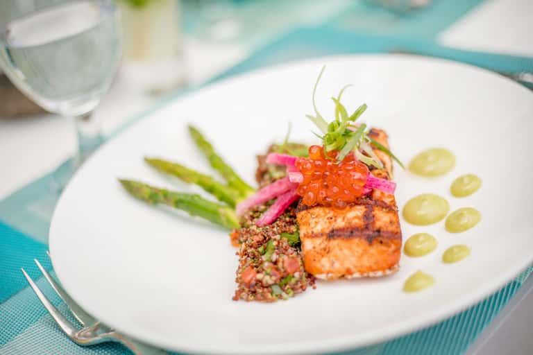 Elegantly plated salmon with asparagus, quinoa, and caviar garnish on white plate