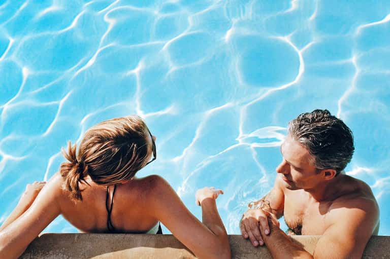Couple relaxing in bright blue swimming pool with rippling water reflections