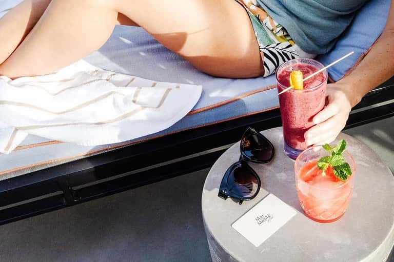 Overhead view of two people lounging by pool with colorful cocktails and sunglasses