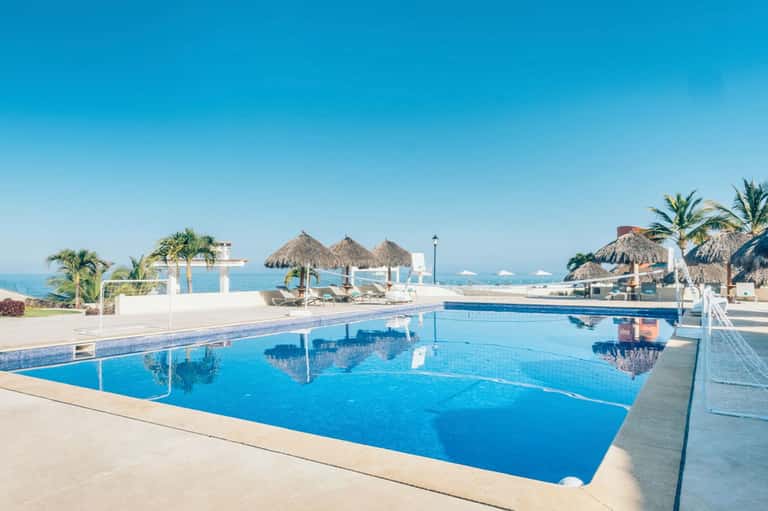Resort infinity pool overlooking turquoise ocean with thatched umbrellas and white loungers