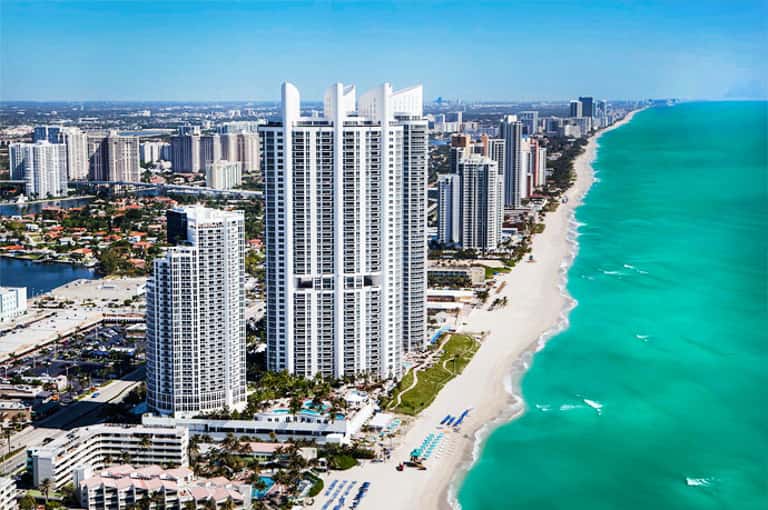 Aerial view of beachfront high-rise resort buildings along turquoise ocean with white sand beach