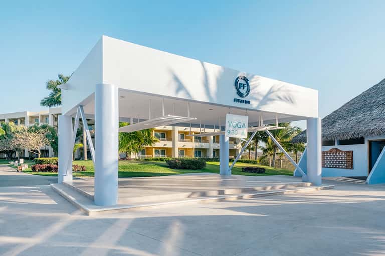 White modern yoga pavilion with X-braced columns and palm trees in tropical resort setting