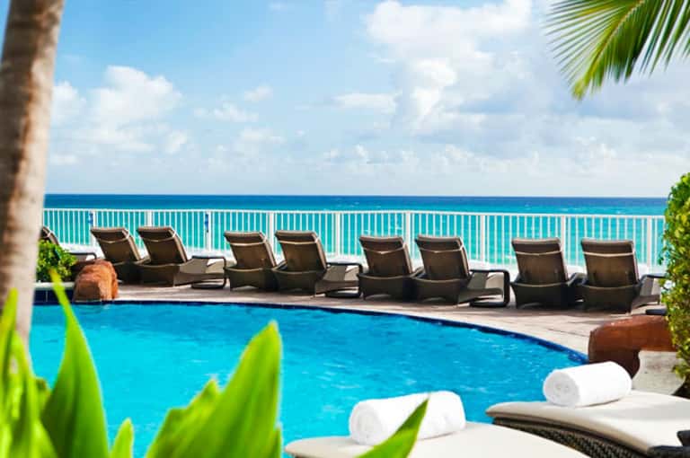 Resort pool with lounge chairs overlooking turquoise ocean and palm trees