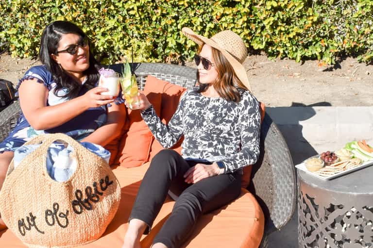 Two women enjoying drinks poolside with vineyard hedge backdrop