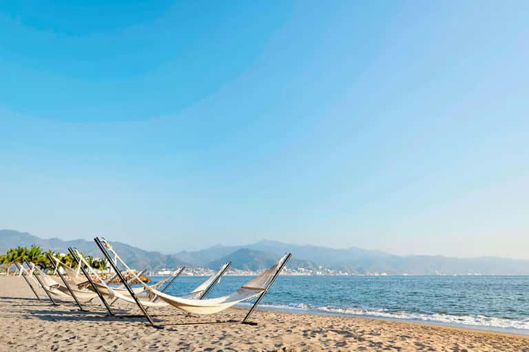 Empty beach loungers facing the ocean with mountains and coastal town in the background