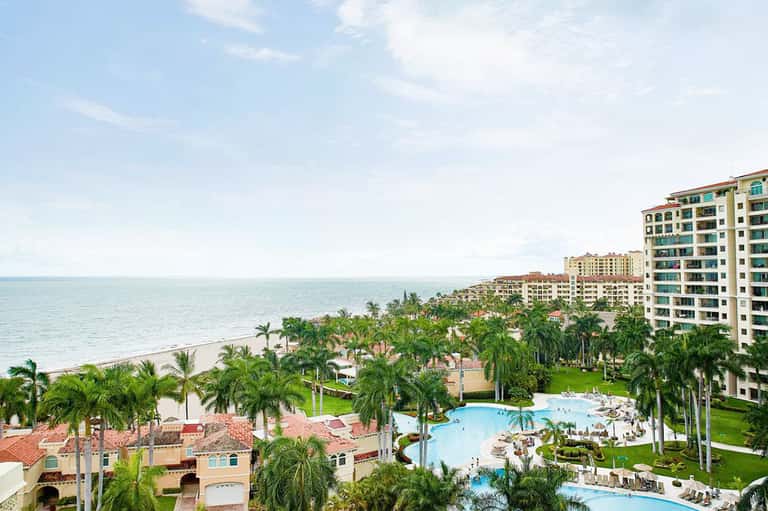 Aerial view of beachfront resort with pools, palm trees, and multi-story buildings along sandy shore