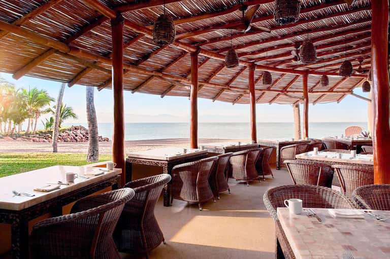 Beachfront dining area with wooden pergola, wicker chairs, and ocean views