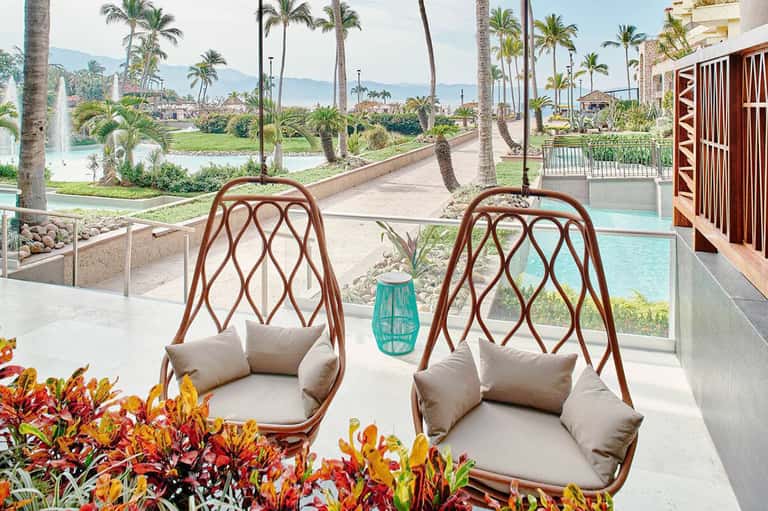 Two woven hanging chairs with cushions overlooking tropical resort grounds and golf course