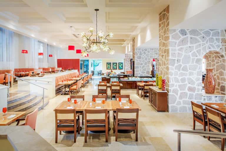 Spacious modern restaurant and lounge with coral seating, geometric stone walls, and hanging light fixtures