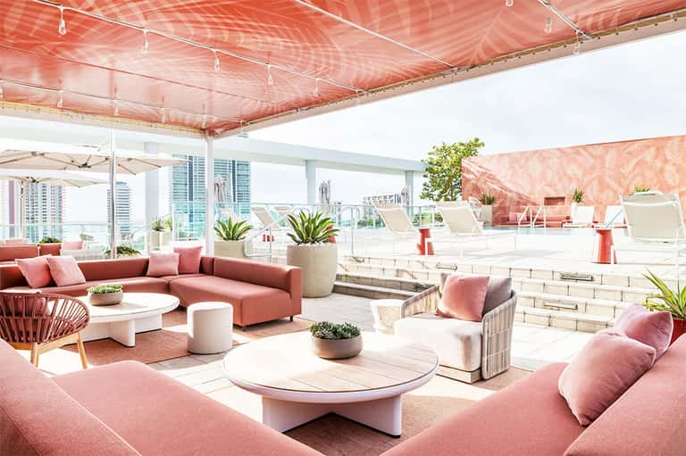 Contemporary rooftop lounge with coral seating, red retractable awning, city skyline views