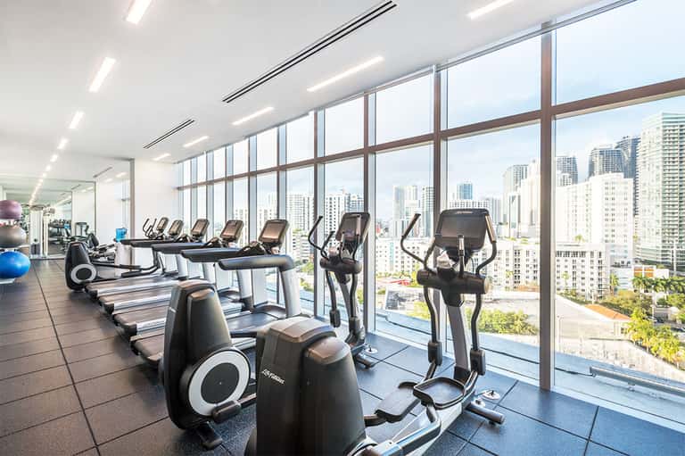 Modern gym with cardio equipment and floor-to-ceiling windows overlooking city skyline