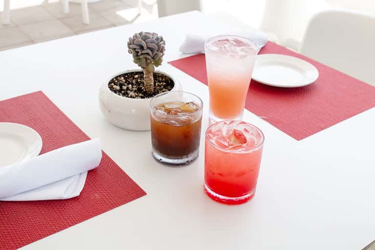 Dining table set with pink napkins, white plates, small potted succulent, and colorful cocktails