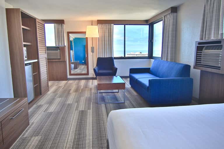 Modern hotel suite with blue sofa, ocean view windows, wood furnishings, and contemporary décor