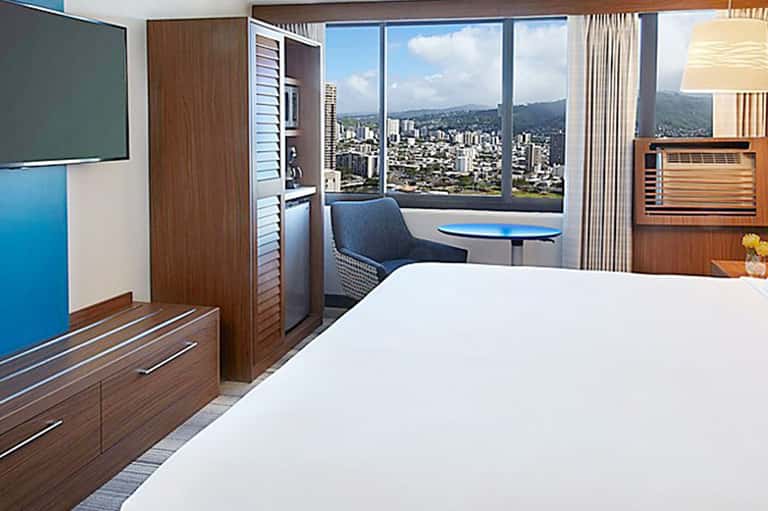 Modern hotel room with city skyline view through floor-to-ceiling windows, wood furnishings, and workspace