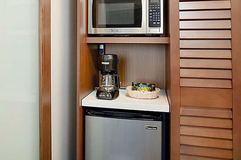 Hotel room kitchenette with microwave, coffee maker, mini refrigerator, and wooden cabinetry