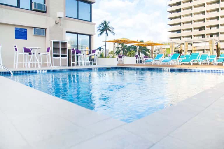 Resort pool with turquoise water, lounge chairs, palm tree, and high-rise buildings
