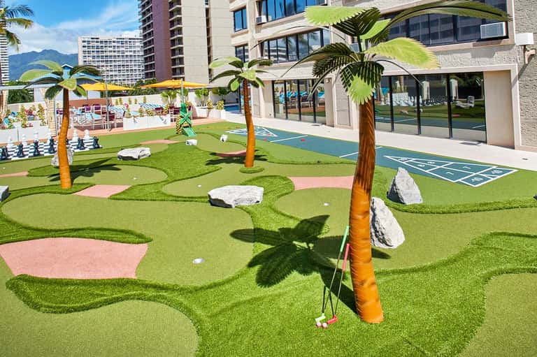 Miniature golf course with palm trees and colorful fairways at a resort with high-rise buildings