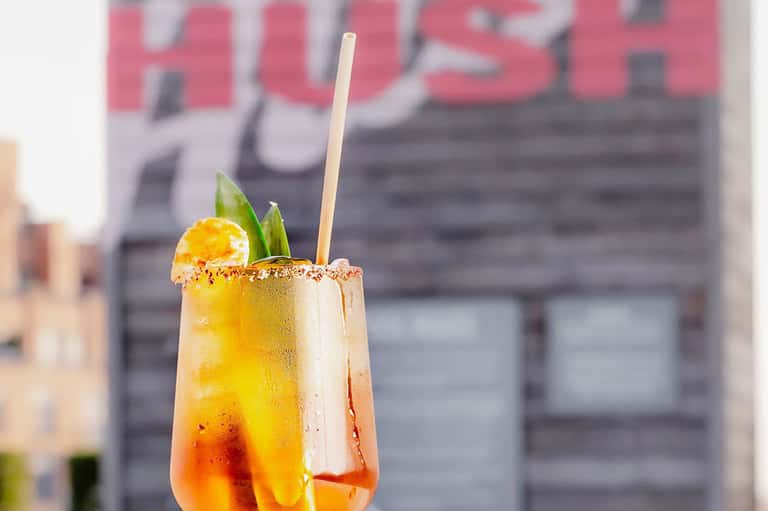 Colorful tropical cocktail with spicy rim in urban setting with blurred signage