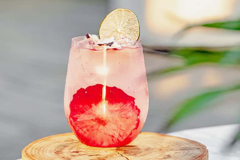 Pink grapefruit cocktail with lime wheel garnish on wooden surface