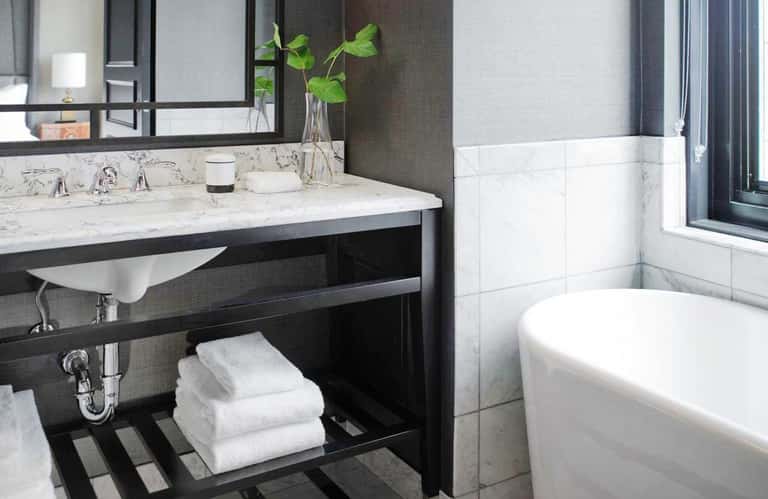 Contemporary bathroom with black vanity, marble countertop, white soaking tub, and large mirror