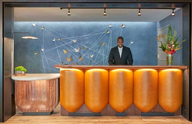 Modern hotel lobby with blue accent wall, gold cylindrical sculptural elements, and wooden reception desk