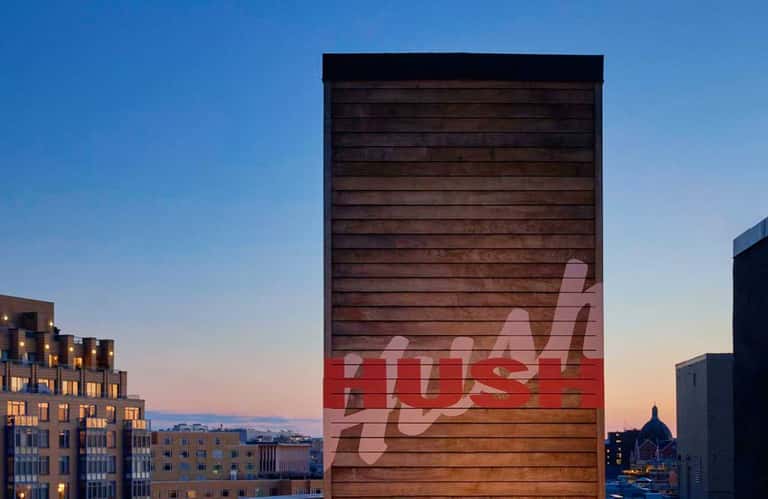 Modern wooden building facade with red 'JUST' text at dusk with city lights