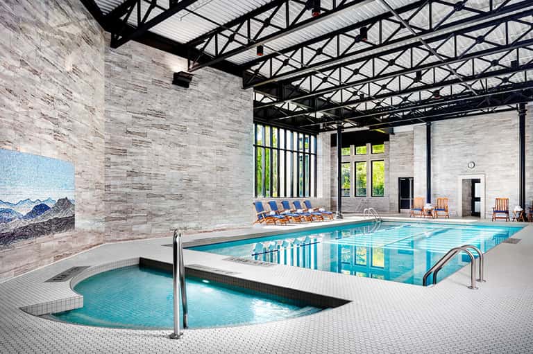 Indoor aquatic center with lap pool, hot tub, lounge chairs, and modern architectural design