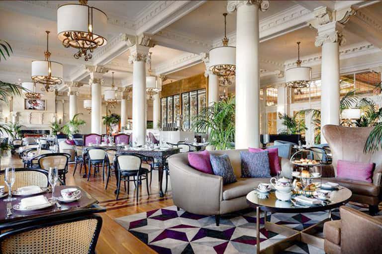 Elegant hotel lobby with white columns, ornate chandeliers, and purple accent chairs