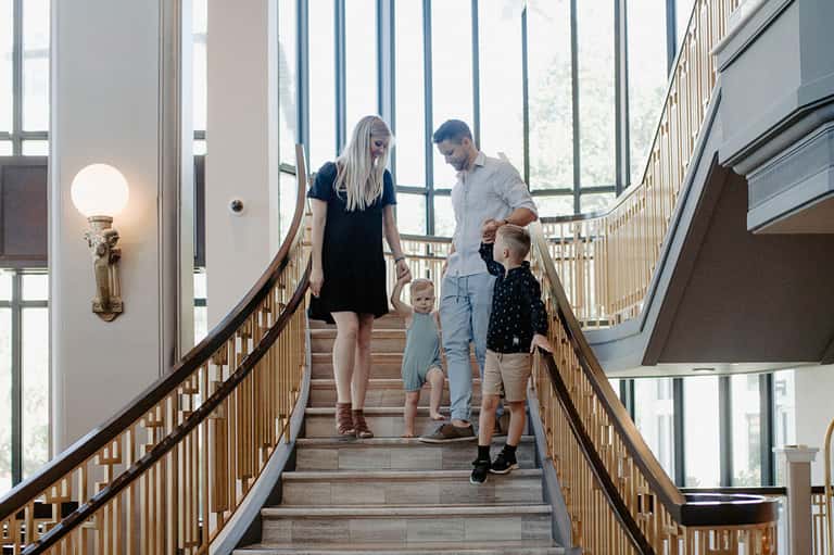 Family of four descending modern staircase with natural light and wooden railings in contemporary hotel lobby