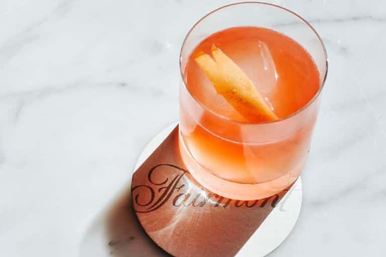 Coral-colored cocktail with citrus garnish on a marble surface with resort branding