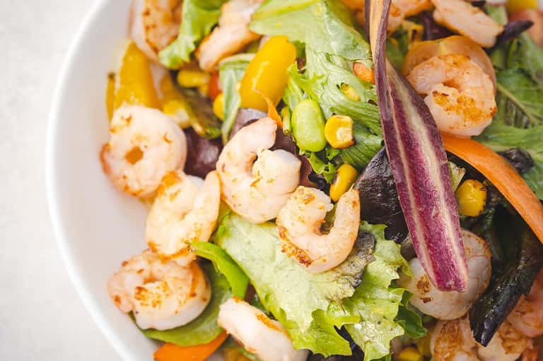 Gourmet shrimp salad with greens, corn, and purple vegetables on white plate
