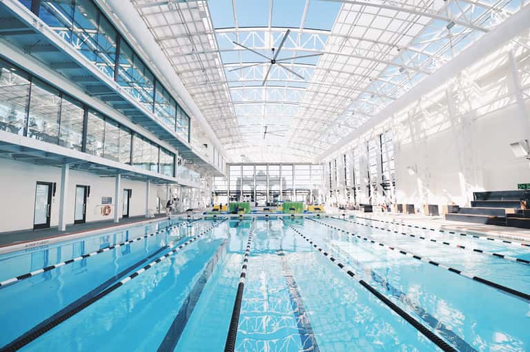 Indoor Olympic-size swimming pool with lane dividers under glass ceiling in modern facility