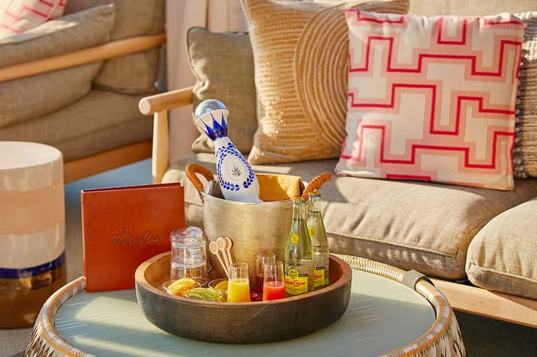 Elegant living room detail with decorative pillows, woven side table, and styled coffee table with beverages