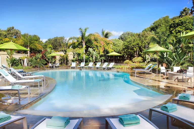 Resort pool with tropical landscaping, loungers, and green umbrellas surrounded by lush gardens