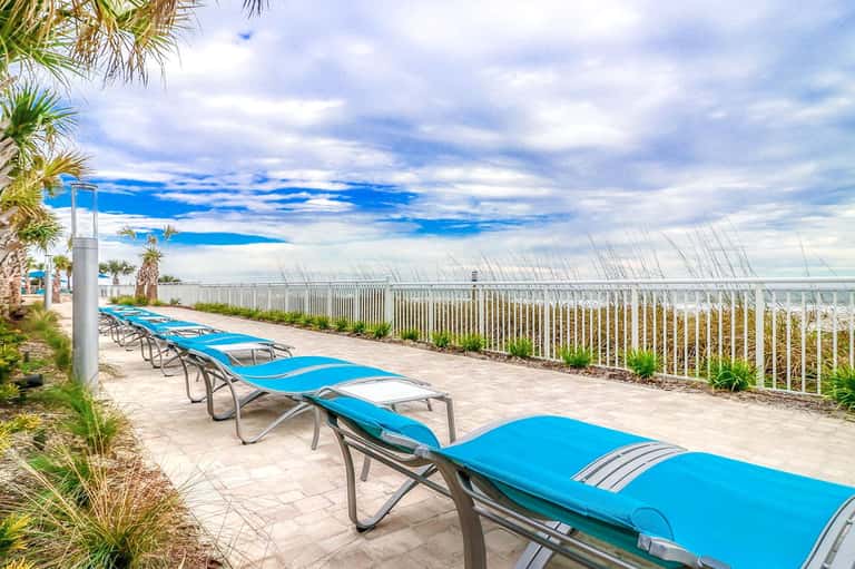 Blue lounge chairs lined up on patio with ocean view and white fence railing