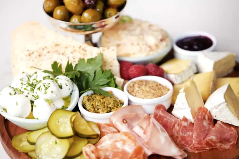 Gourmet charcuterie and cheese board with olives, cured meats, crackers, pickles, and condiments