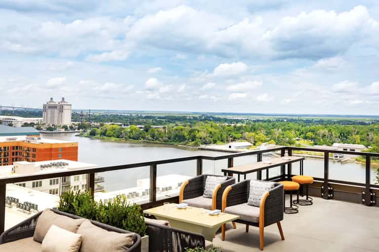 Rooftop terrace with lounge seating overlooking a river and distant landscape under cloudy sky