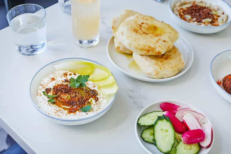 Mediterranean breakfast spread with hummus, pita bread, fresh vegetables, and beverages