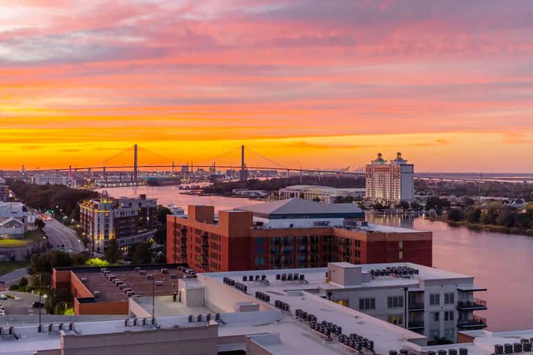 Waterfront cityscape at sunset with industrial bridges and riverside buildings in warm golden light